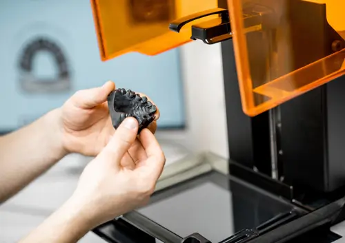 Dental technician holding a 3D-printed black resin surgical guide for precise implant placement.