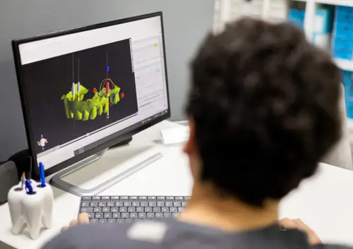 Smiling patient in glasses looks in mirror at dental results while assistant smiles in background.