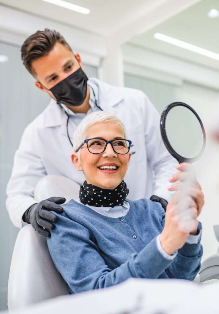 Beautiful senior woman having dental treatment at dentist's office. Dentist is wearing protective face mask due to coronavirus pandemic.