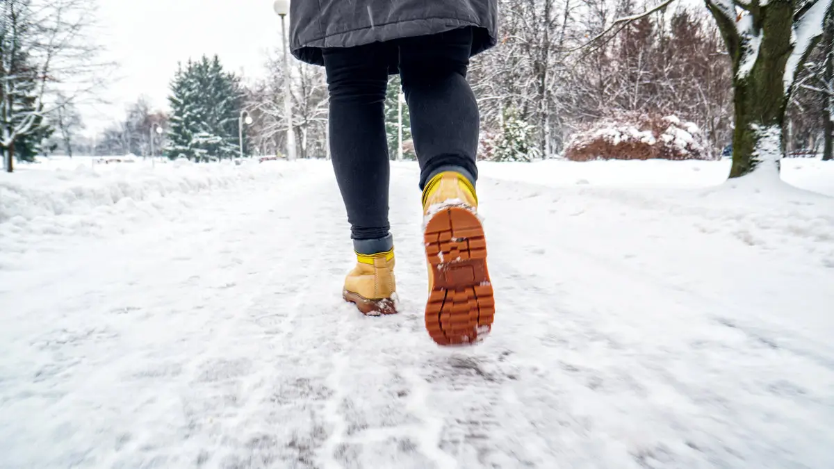 Winter Walk in Yellow Leather Boots. Back view on the feet of a women walking along the icy snowy pavement. Pair of shoe on icy road in winter. Abstract empty blank winter weather background