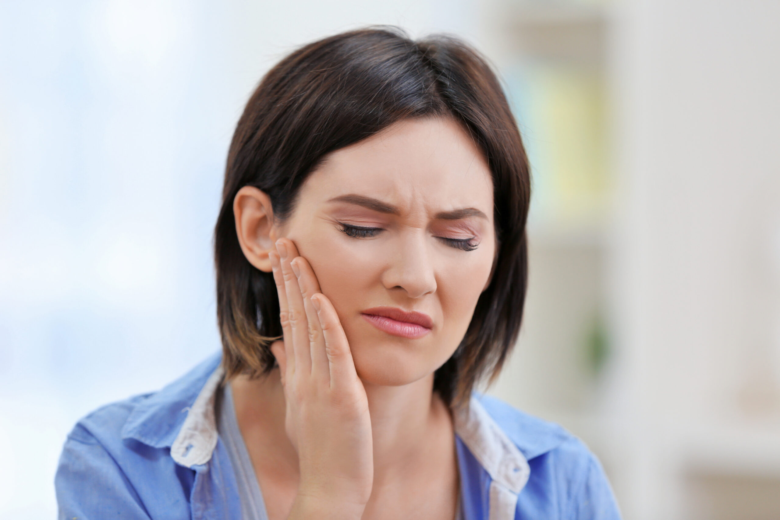 Young woman holding her jaw in discomfort at home